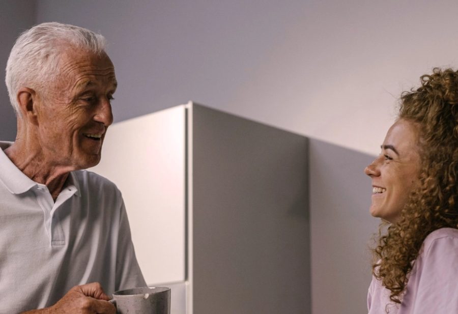 Senior steht mit einer Tasse in der Küche und unterhält sich mit einer Betreuungskraft