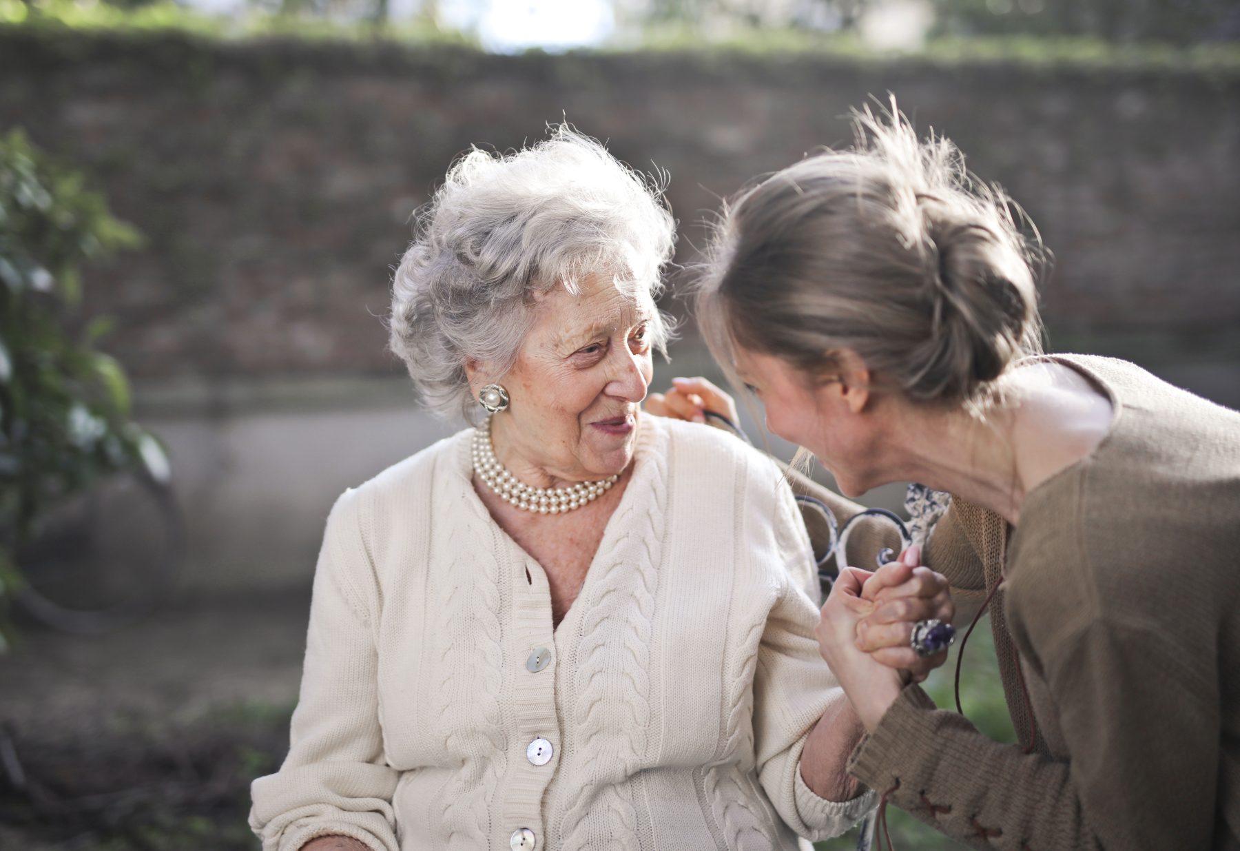 Seniorin sitzt im Garten und wird von einer Betreuungskraft an der Hand gehalten