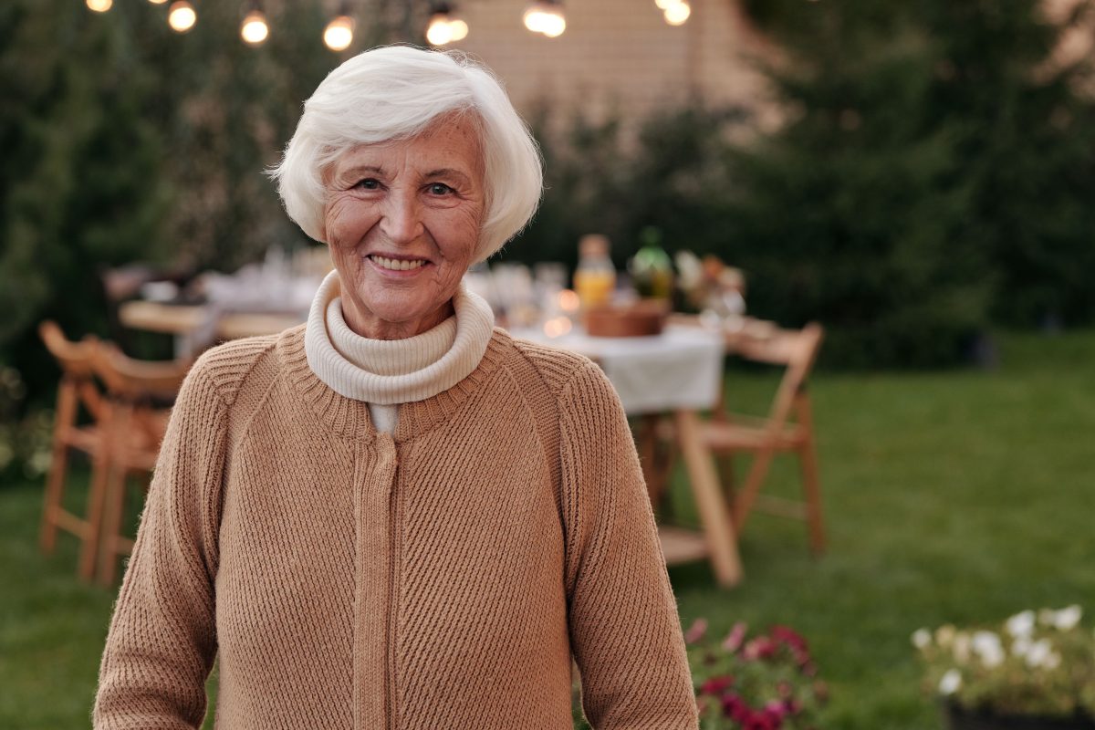 Lächelnde Seniorin im Garten, im Hintergrund ein gedeckter Tisch