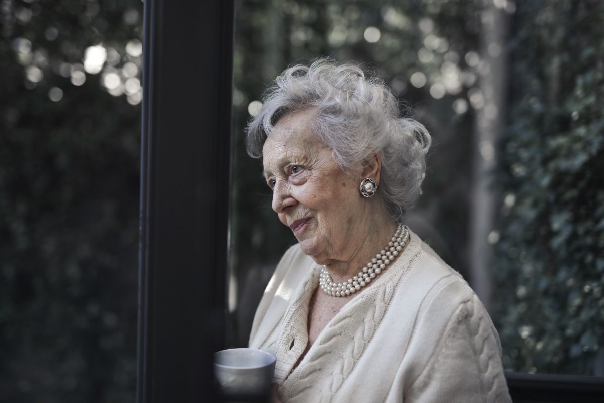 Seniorin mit einer Tasse Kaffee am Fenster ihrer Wohnung